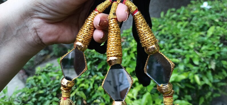 May include: Three gold tassel ornaments with small diamond-shaped mirrors. Each tassel has a gold cord and a red and gold tassel.