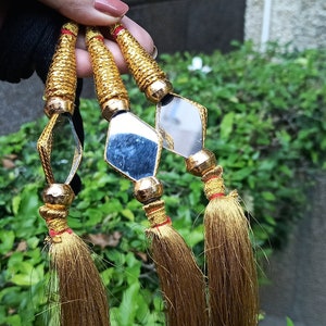 May include: Three gold tassel ornaments with diamond-shaped mirrors. The mirrors have a reflective surface and are attached to the tassels with gold beads.