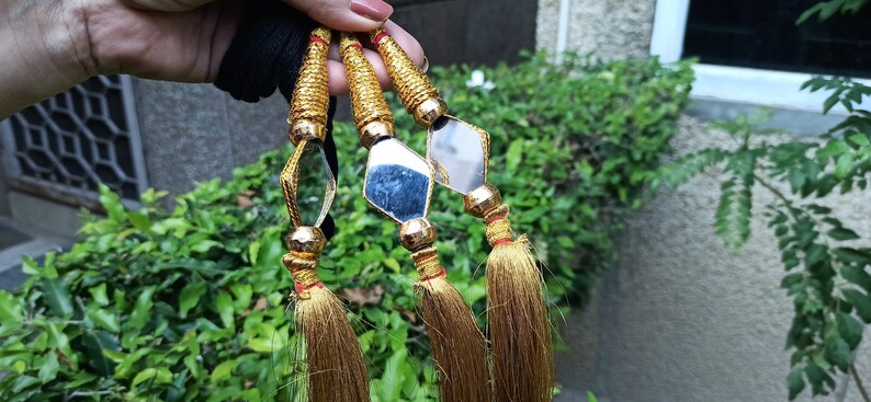 May include: Three gold tassel ornaments with diamond-shaped mirrors. The mirrors have a reflective surface and are attached to the tassels with gold beads.