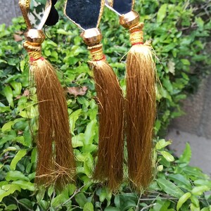 May include: Three gold tassels with black and gold accents hanging from a dark blue background.