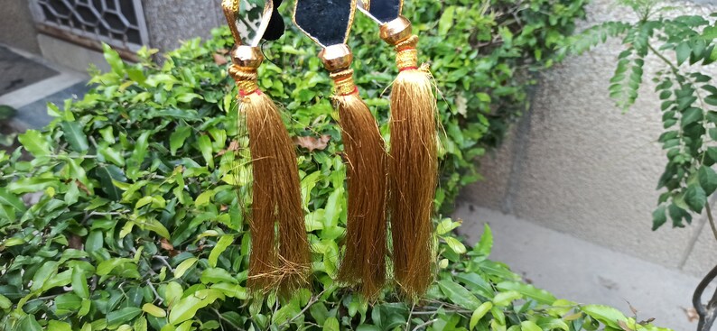 May include: Three gold tassels with black and gold accents hanging from a dark blue background.