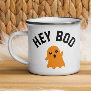 May include: White enamel mug with a black rim and a black and orange ghost graphic. The text 