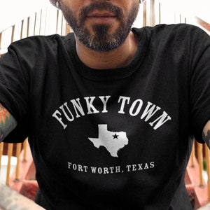 May include: Black t-shirt with white text that reads "Funky Town" and a white outline of the state of Texas with a star in the center. Below the state outline is the text "Fort Worth, Texas."