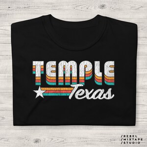 Może przedstawiać: Czarny T-shirt z retro grafiką, która głosi "Temple Texas" w kolorowych paskach i gwiazdą.