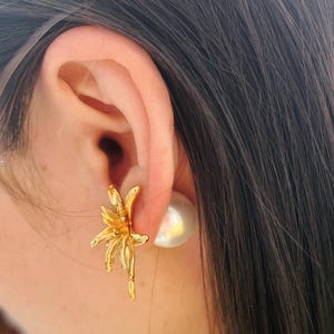May include: A close-up of a person's ear wearing a gold flower-shaped earring and a white pearl earring.
