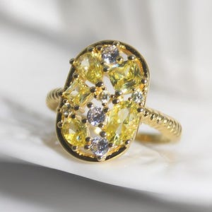 May include: A gold ring with a large oval-shaped setting filled with small yellow and white gemstones.