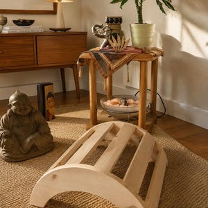 May include: A light-coloured wooden back stretcher featuring a curved, arched frame with five parallel slats. The device has a semi-circular profile with solid side panels, designed for spinal support and stretching exercises on the floor.