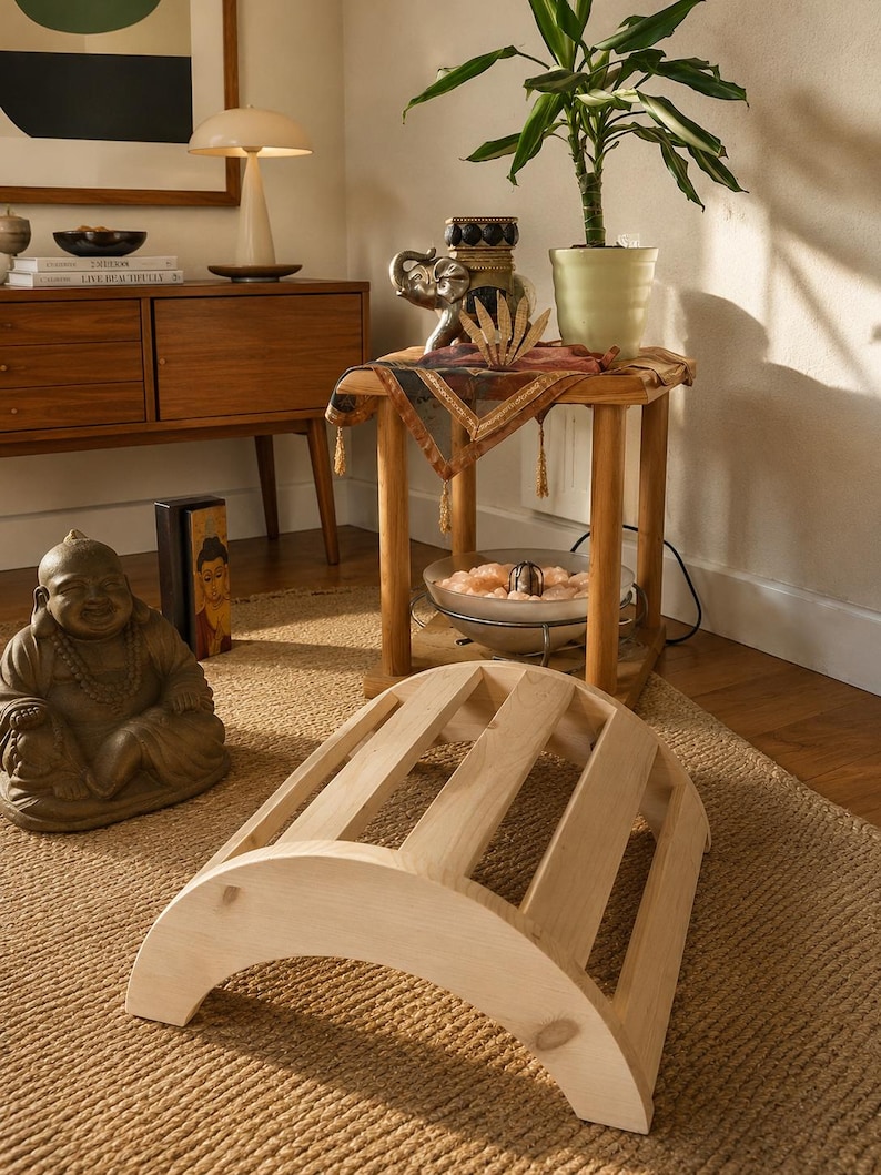 May include: A light-coloured wooden back stretcher featuring a curved, arched frame with five parallel slats. The device has a semi-circular profile with solid side panels, designed for spinal support and stretching exercises on the floor.