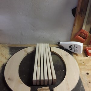 May include: A set of unfinished light-coloured wooden components including two large semi-circular arcs, five rectangular slats, and ten small cylindrical dowels arranged on a flat surface next to a white plastic bottle of Ponal wood glue.