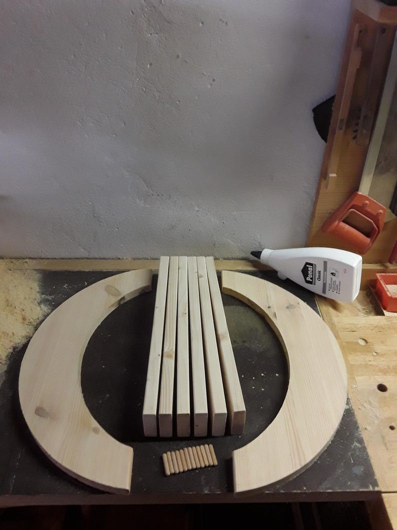 May include: A set of unfinished light-coloured wooden components including two large semi-circular arcs, five rectangular slats, and ten small cylindrical dowels arranged on a flat surface next to a white plastic bottle of Ponal wood glue.