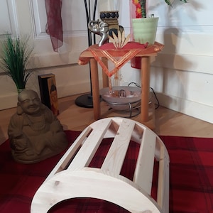 May include: A wooden arch-shaped back support with five slats. The support is made of light-colored wood and is sitting on a red and black checkered rug.