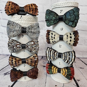 May include: A display of nine feather bow ties in various colors and patterns. The bow ties are arranged on two white stands with rope trim. The stands are labeled with letters A through I.