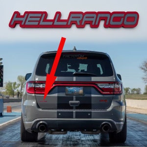 Può includere: Un Dodge Durango grigio con un adesivo a strisce nere e grigie sul retro. L'auto ha un emblema "HELLRANGO" in alto e un adesivo "FACTOTUM Motorsports" sul lunotto posteriore. La targa recita "FMS GEAR".