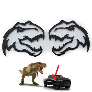May include: Two black and white dinosaur head decals with red eyes. The decals are facing each other with their mouths open. A black pickup truck with a red arrow pointing to the hood. A brown dinosaur is standing in front of the truck.