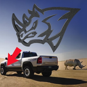 Può includere: Un pick-up bianco con un logo di rinoceronte nero sul lato. Il camion è parcheggiato in un ambiente desertico con un rinoceronte sullo sfondo.