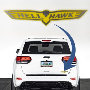May include: A white Jeep Cherokee with a yellow and silver "Hellhawk" decal on the rear. The decal is a stylised bird with wings outstretched. The Jeep has a number plate that reads "FMS GEAR".