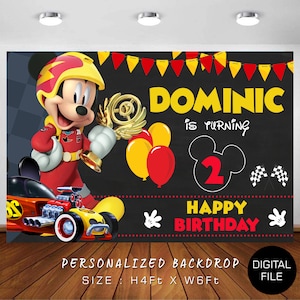May include: A personalised birthday backdrop featuring Mickey Mouse dressed as a race car driver holding a trophy. The backdrop is black with red, yellow, and white accents. The text "DOMINIC is turning 2 HAPPY BIRTHDAY" is written on the backdrop. The backdrop is 1.2 metres tall and 1.8 metres wide.