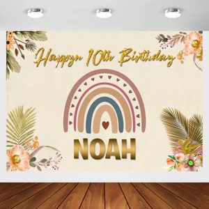 May include: A beige background with a rainbow arch in shades of brown, blue, and pink. The rainbow is decorated with small pink hearts. The text "Happy 10th Birthday" is written in gold glitter letters. The name "NOAH" is written in gold letters below the rainbow.