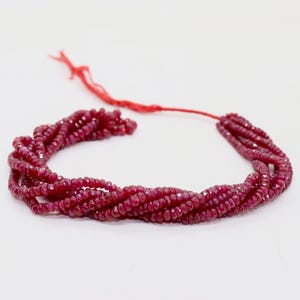 May include: A necklace composed of multiple strands of small, faceted, deep red gemstones. The strands are twisted together, and a red string is attached at the top. The gemstones have a sparkling appearance.