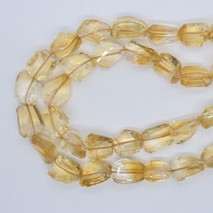 May include: A strand of faceted, golden yellow citrine beads. The beads are all roughly the same size and shape, and they have a smooth, polished finish.