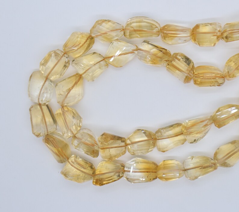 May include: A strand of faceted, golden yellow citrine beads. The beads are all roughly the same size and shape, and they have a smooth, polished finish.