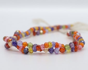 May include: A strand of colorful faceted gemstone beads. The beads are in shades of orange, red, yellow, green, purple, and blue. The beads are strung on a clear thread.
