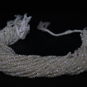 May include: A strand of white moonstone beads with iridescent shimmer. The beads are faceted and have a slightly irregular shape. The strand is approximately 16 inches long.