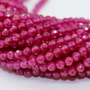 May include: A strand of pink faceted gemstone beads. The beads are round and have a shiny, polished finish.