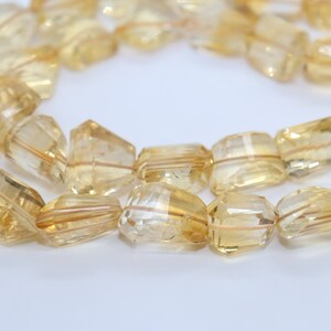 May include: A strand of faceted, golden yellow citrine beads. The beads are rectangular in shape and have a translucent appearance.