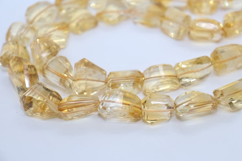 May include: A strand of faceted, golden yellow citrine beads. The beads are rectangular in shape and have a translucent appearance.