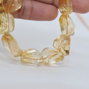May include: A strand of faceted, translucent, golden yellow citrine beads. The beads are irregularly shaped and have a slightly rough texture.