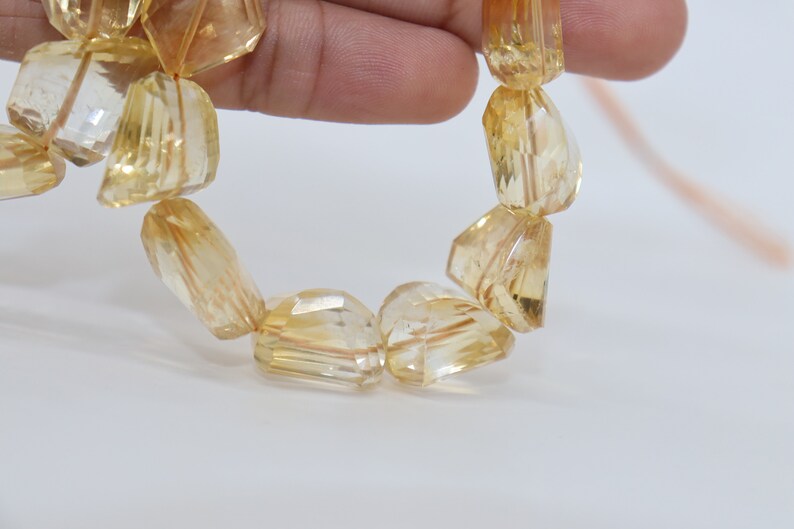 May include: A strand of faceted, translucent, golden yellow citrine beads. The beads are irregularly shaped and have a slightly rough texture.