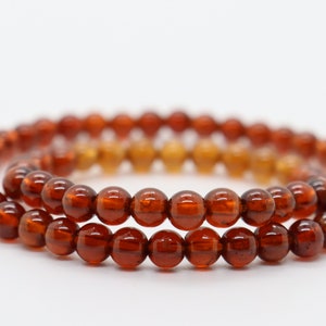 May include: Two strands of brown gemstone beads, each with a round shape, are layered on top of each other. The beads are a deep reddish-brown color and have a glossy finish.
