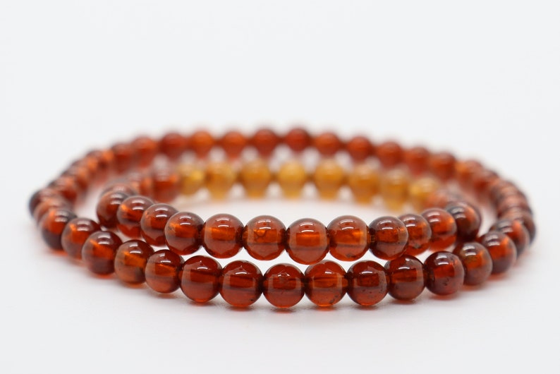 May include: Two strands of brown gemstone beads, each with a round shape, are layered on top of each other. The beads are a deep reddish-brown color and have a glossy finish.