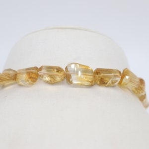 May include: A strand of golden citrine beads, each bead is faceted and has a unique shape. The beads are strung on a clear elastic cord and are ready to be made into a necklace or bracelet.