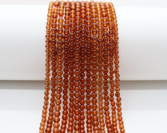 May include: A strand of round, orange carnelian beads. The beads are smooth and polished, and they are strung on a clear thread.