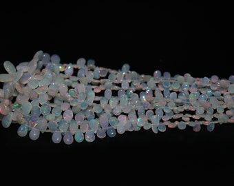 May include: Strands of iridescent opal beads. The beads are teardrop-shaped and vary in size, strung together to create a shimmering effect. The opals display flashes of color against a dark background.