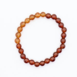 May include: A brown gemstone bracelet with round beads. The beads are a gradient of brown, with the lighter brown beads at the top and the darker brown beads at the bottom.
