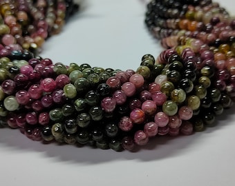 May include: A strand of multi-colored round beads, featuring shades of green, pink, and black. The beads are made of natural gemstone and are strung together on a clear thread.