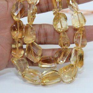 May include: A strand of faceted, golden citrine beads. The beads are a light yellow color and have a translucent appearance. The beads are strung on a clear string.