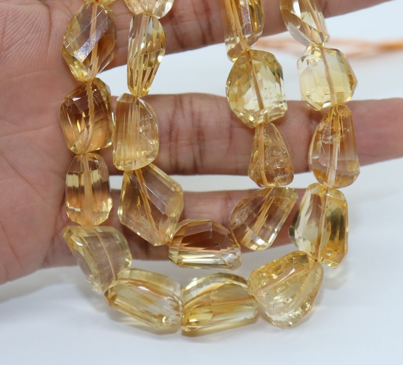 May include: A strand of faceted, golden citrine beads. The beads are a light yellow color and have a translucent appearance. The beads are strung on a clear string.