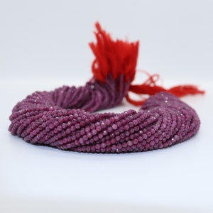 Puede incluir: Una hebra de cuentas de piedras preciosas facetadas de color rojo rubí. Las cuentas son pequeñas y redondas, y están enhebradas en un hilo. Las cuentas están dispuestas en círculo, y todas son del mismo tamaño y forma.