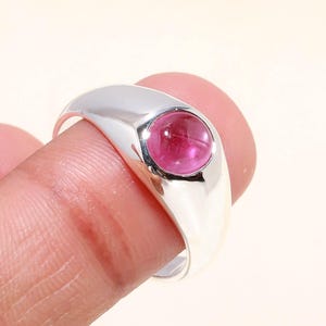 Peut inclure: Une bague en argent poli avec une pierre précieuse rose vif et ronde. La bague a un anneau lisse et arrondi et un sertissage à lunette. La pierre précieuse est le point central, attirant la lumière et ajoutant une touche de couleur.