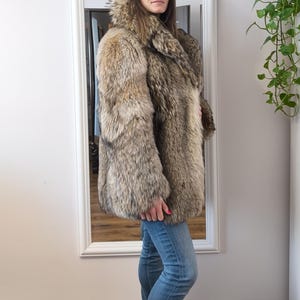 K&ouml;nnte beinhalten: Ein Pelzmantel in voller L&auml;nge mit gro&szlig;em Kragen. Der Mantel hat eine Mischung aus Braun- und Graut&ouml;nen. Die Person tr&auml;gt blaue Jeans und schwarze Stiefeletten. Der Mantel wirkt warm und luxuri&ouml;s.