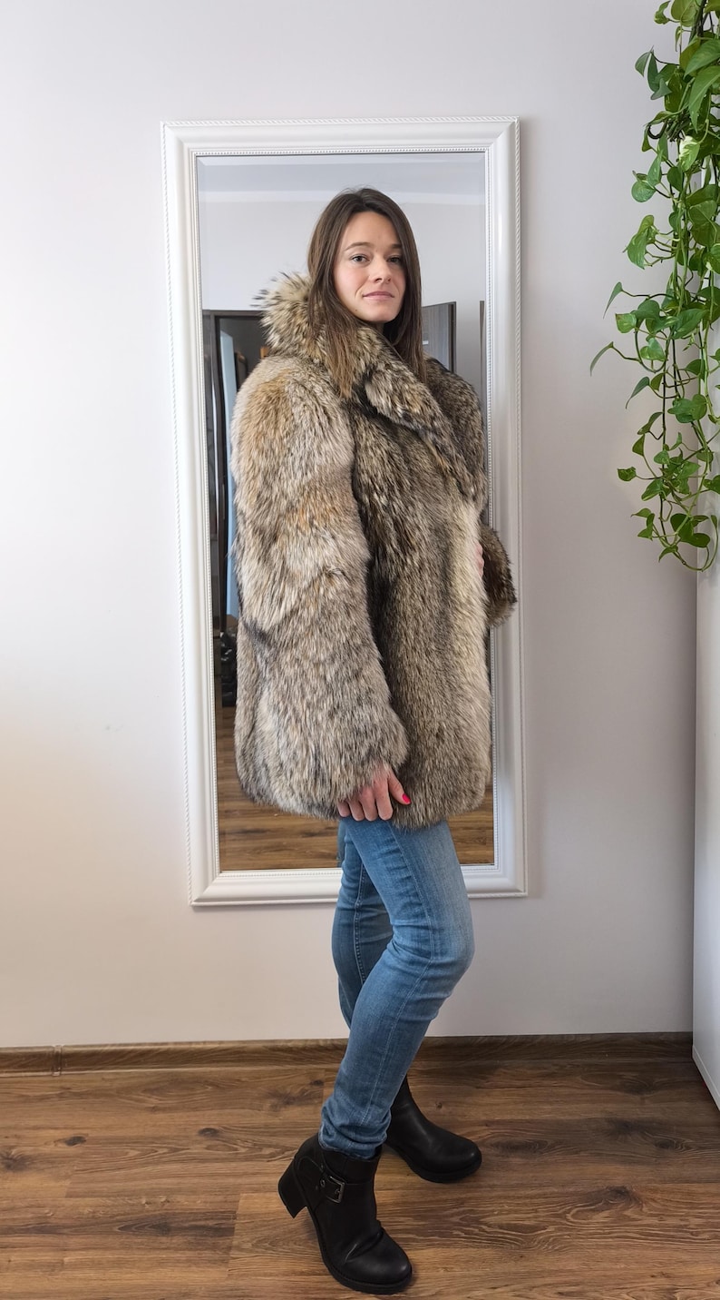 K&ouml;nnte beinhalten: Ein Pelzmantel in voller L&auml;nge mit gro&szlig;em Kragen. Der Mantel hat eine Mischung aus Braun- und Graut&ouml;nen. Die Person tr&auml;gt blaue Jeans und schwarze Stiefeletten. Der Mantel wirkt warm und luxuri&ouml;s.