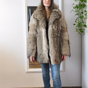 K&ouml;nnte beinhalten: Ein Vintage-Pelzmantel in Braun- und Graut&ouml;nen. Der Mantel hat einen breiten Kragen und eine klassische Silhouette. Die Person tr&auml;gt eine blaue Jeans und schwarze Stiefel. Der Mantel scheint in gutem Zustand zu sein.