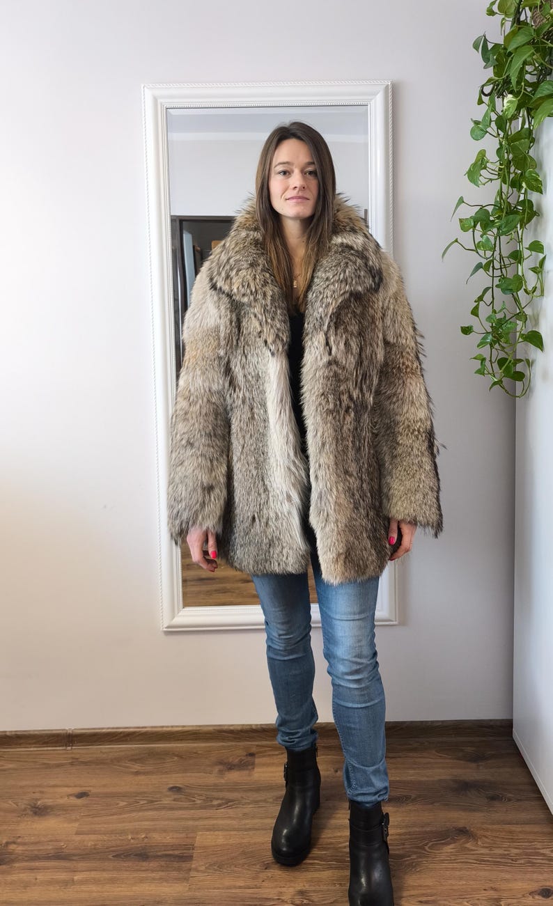 K&ouml;nnte beinhalten: Ein Vintage-Pelzmantel in Braun- und Graut&ouml;nen. Der Mantel hat einen breiten Kragen und eine klassische Silhouette. Die Person tr&auml;gt eine blaue Jeans und schwarze Stiefel. Der Mantel scheint in gutem Zustand zu sein.
