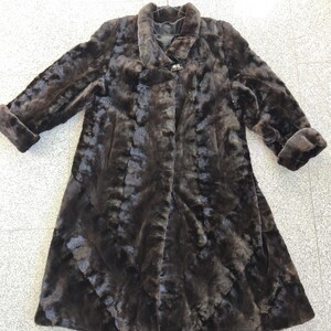 Puede incluir: Un abrigo de piel marr&oacute;n oscuro con un dise&ntilde;o cl&aacute;sico. El abrigo presenta un cuello ancho, mangas largas con pu&ntilde;os vueltos y cierre de bot&oacute;n. El abrigo est&aacute; hecho de un material suave y texturizado.