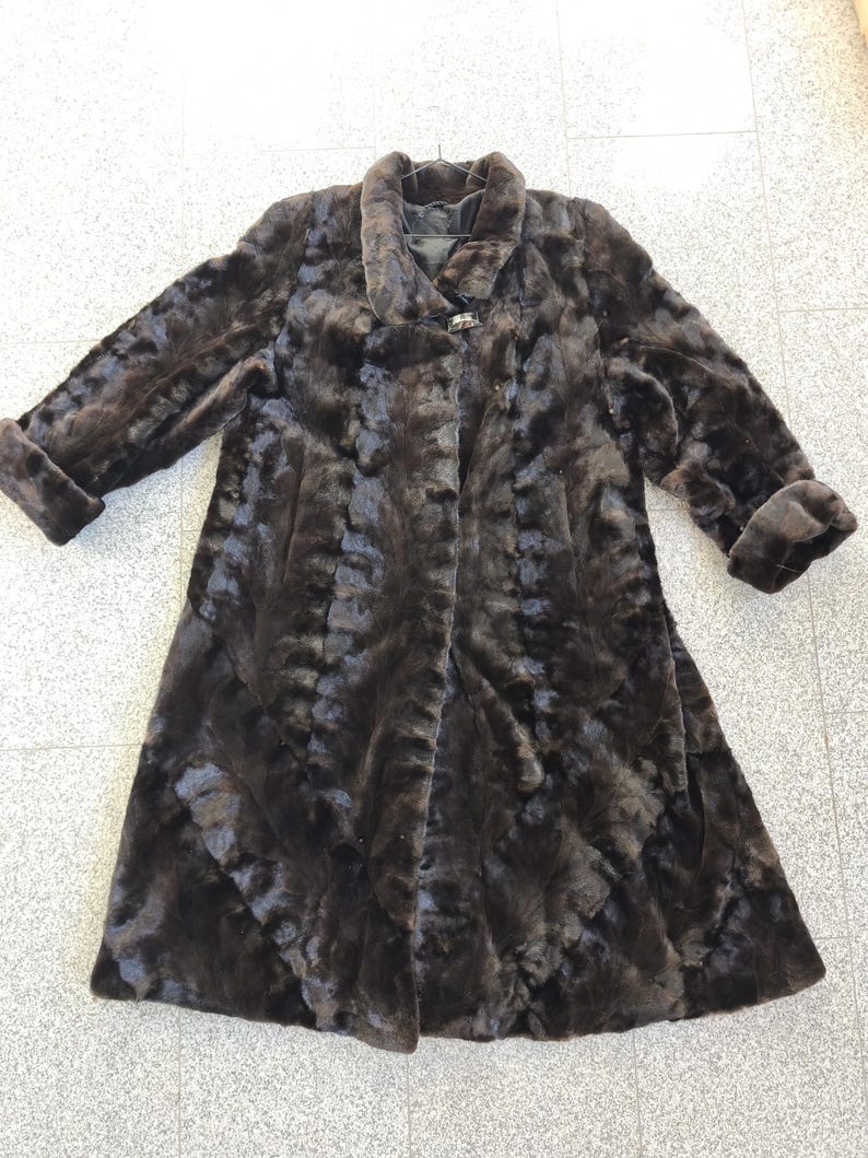 Puede incluir: Un abrigo de piel marr&oacute;n oscuro con un dise&ntilde;o cl&aacute;sico. El abrigo presenta un cuello ancho, mangas largas con pu&ntilde;os vueltos y cierre de bot&oacute;n. El abrigo est&aacute; hecho de un material suave y texturizado.