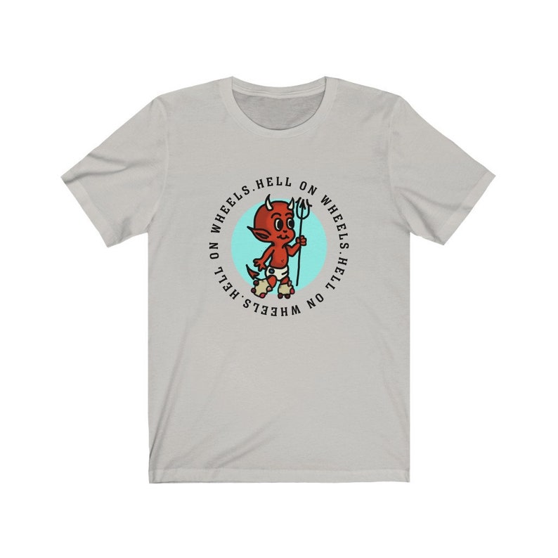 May include: Light gray t-shirt featuring a cartoon devil with a trident, roller skates, and the text "HELL ON WHEELS" in a circular design. The devil is red with white horns and a diaper. The shirt is made of a soft material.